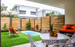 Un patio trasero con piscina, un comedor con mesa y sillas, y una zona de estar con una silla y una sombrilla.