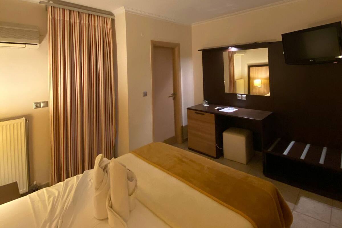 A hotel room with a bed, a desk, a mirror, a television, and an air conditioning unit.