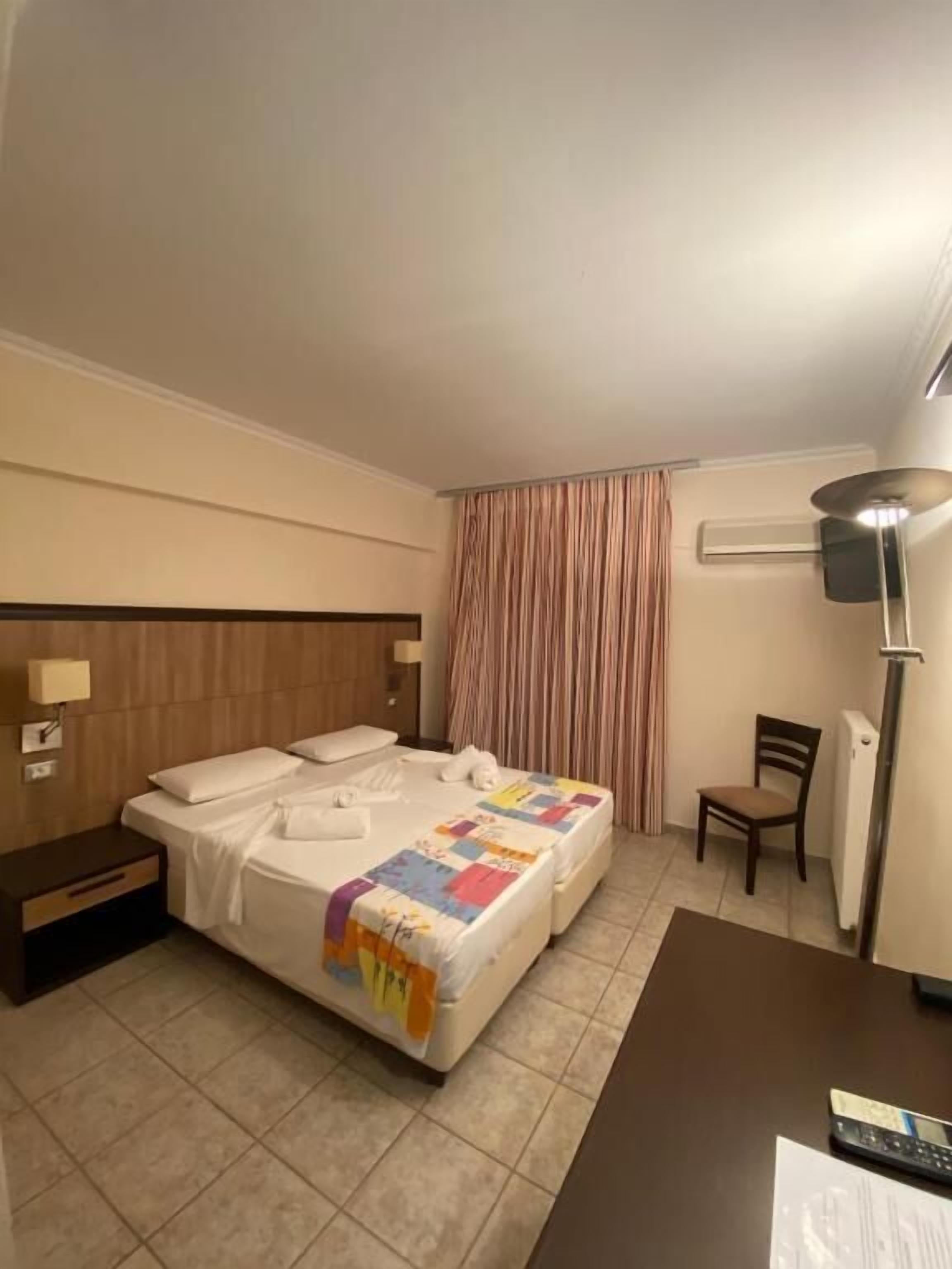 A hotel room with a double bed, a nightstand, a chair, a desk, and a lamp.