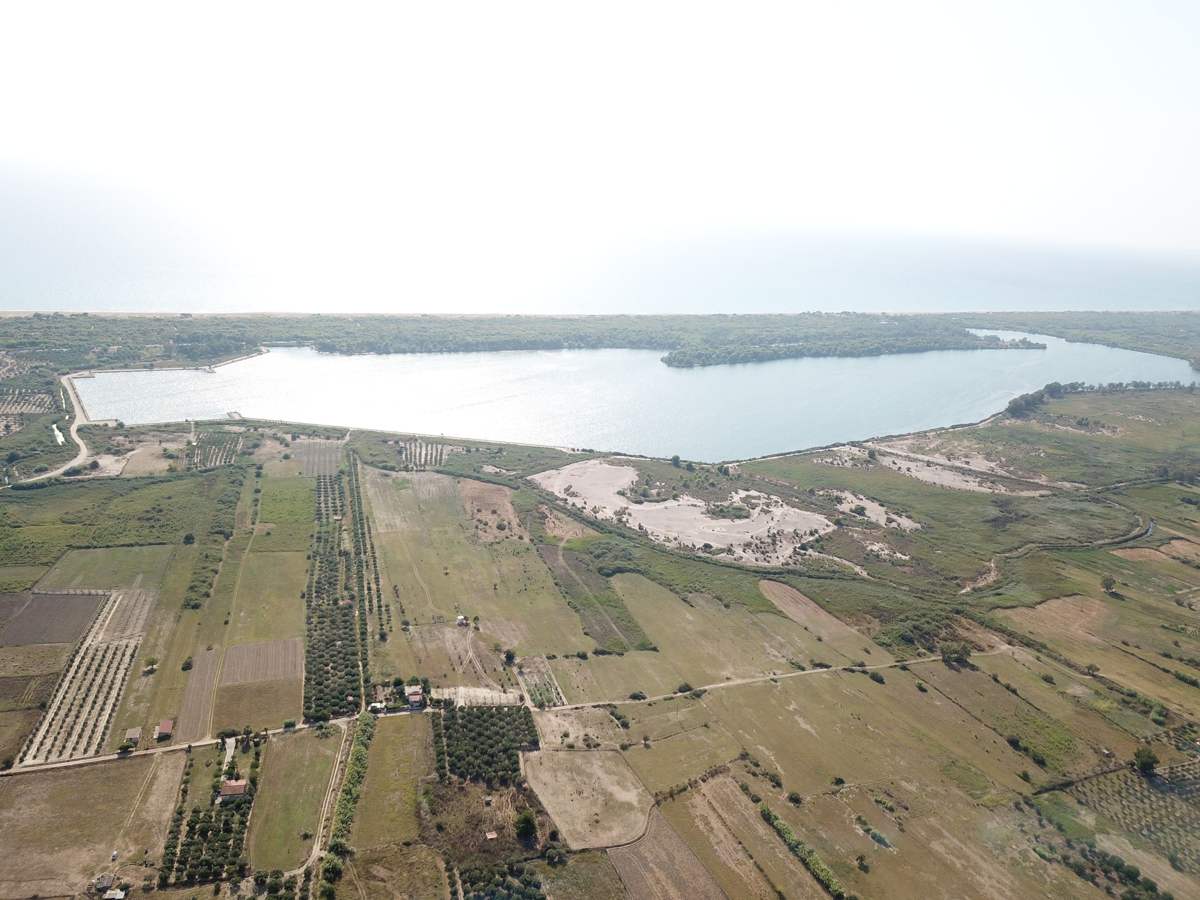 An aerial view of a coastal area with fields, a large body of water, and a small island.