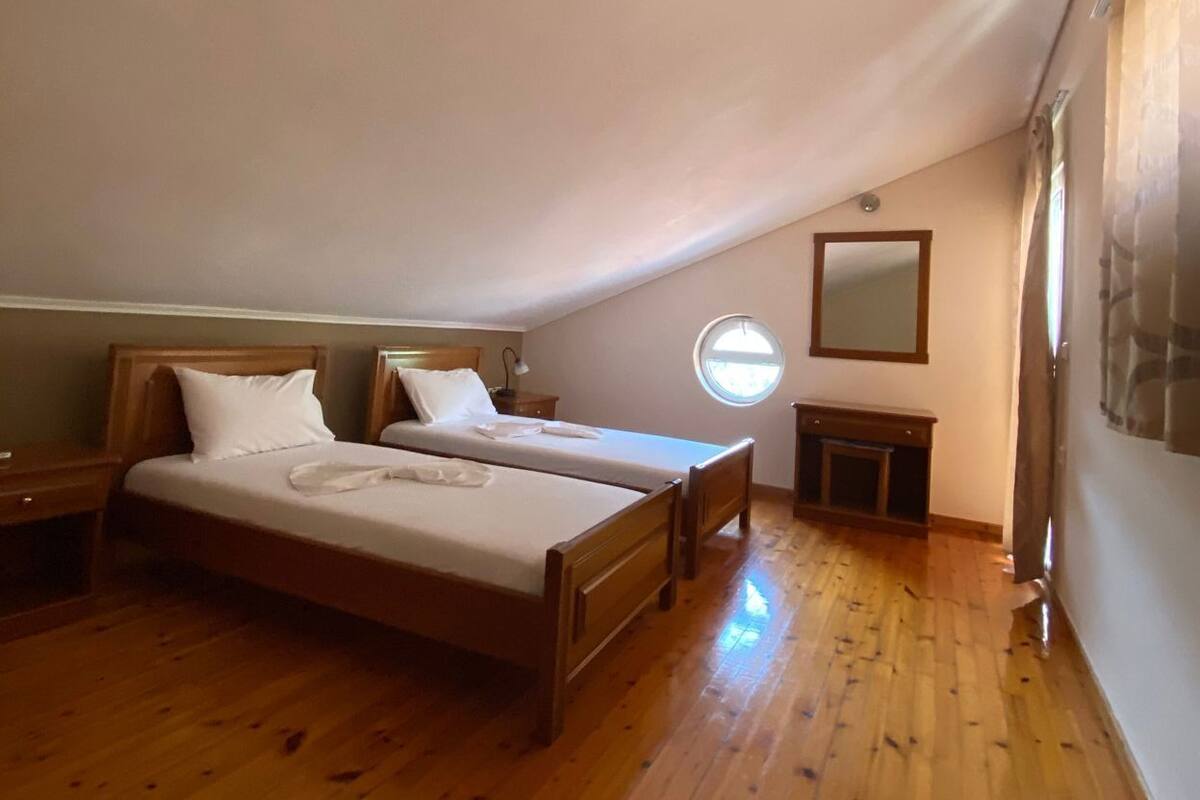A bedroom with two wooden beds, a round window, a mirror, and a wooden floor.
