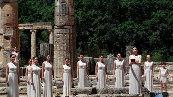 Un groupe de personnes vêtues de robes blanches se tient debout dans les ruines d’un ancien édifice, avec des colonnes et des marches en pierre.