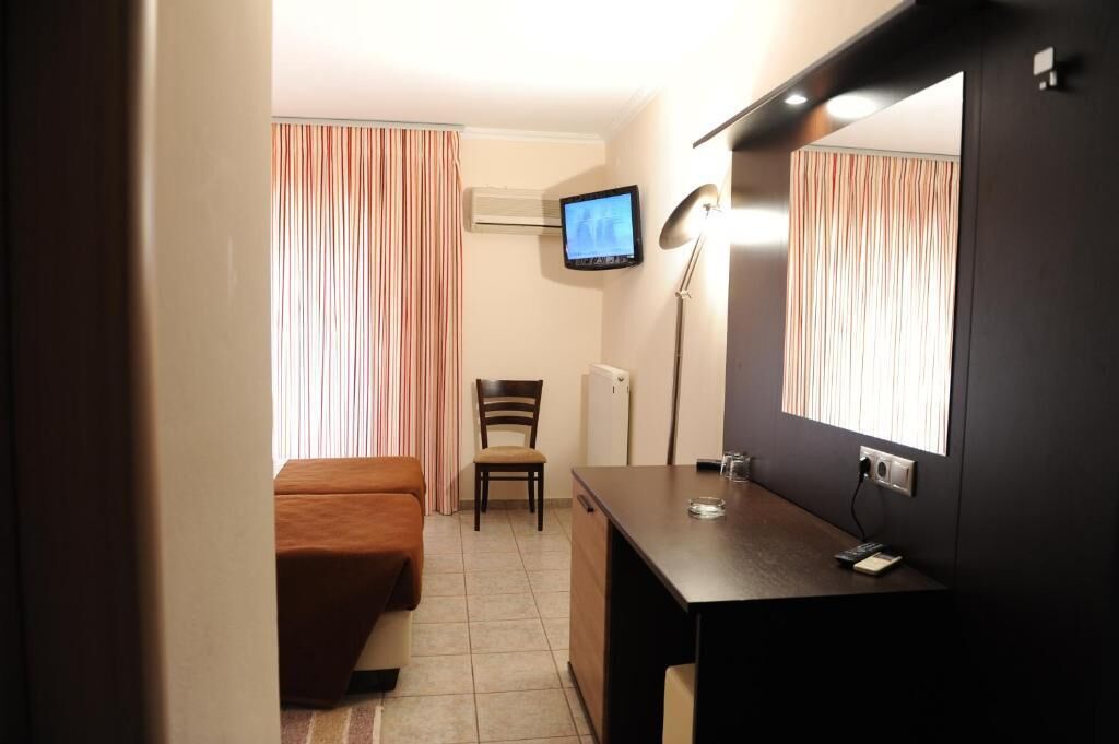 Ein Hotelzimmer mit Bett, Schreibtisch, Stuhl, Fernseher und einem fensterbepflanzten Fenster.