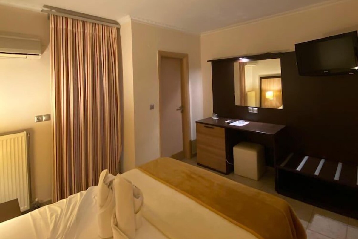 A hotel room with a bed, a desk with a mirror, a television, and a window with curtains.