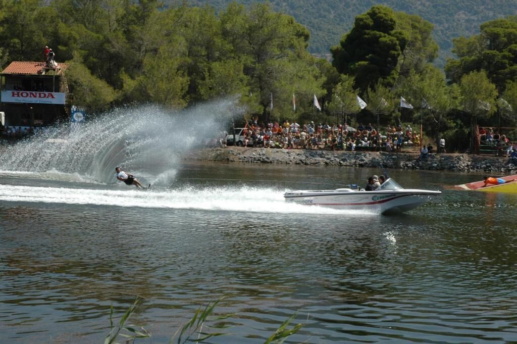 A water sport event with a person wakeboarding on a boat, spectators in the background, and a building with a 'HONDA' sign.