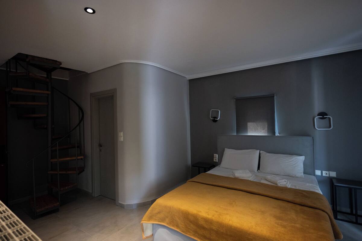A bedroom with a bed, a headboard, a nightstand, a wall-mounted light, and a spiral staircase.