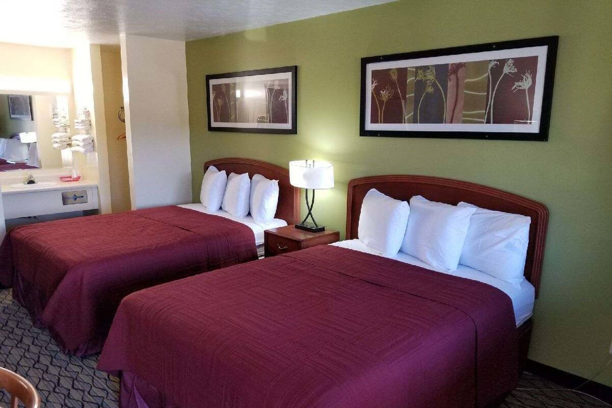 Ein Hotelzimmer mit zwei Betten, einem Schreibtisch mit Lampe und Bildern an den Wänden.