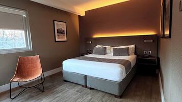 A modern bedroom with a large bed, a chair, and a nightstand.
