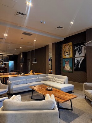 A modern lounge area with a sectional sofa, a wooden coffee table, and a bar area in the background. - Hotel Curicó (Curicó)