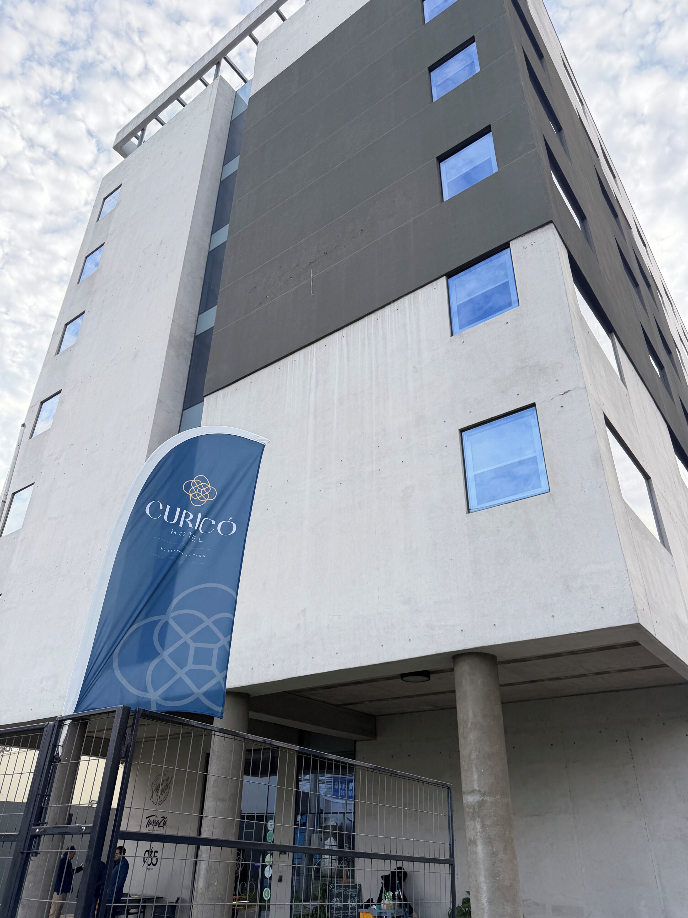 A modern hotel building with a prominent blue banner displaying the hotel name.
