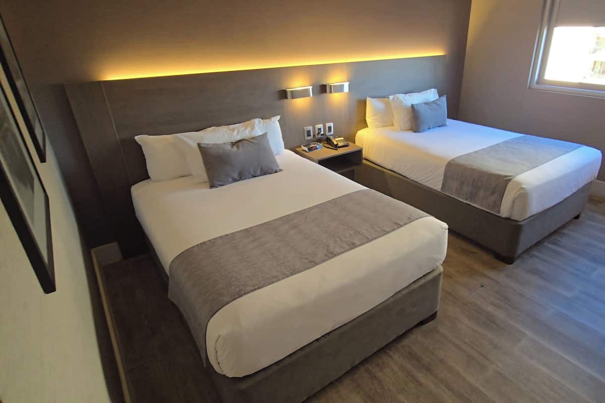 Una habitación de hotel con dos camas, mesitas de noche, un teléfono y una ventana.