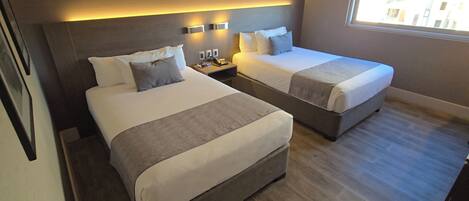 A hotel room with two beds, bedside tables, a phone, and a window.