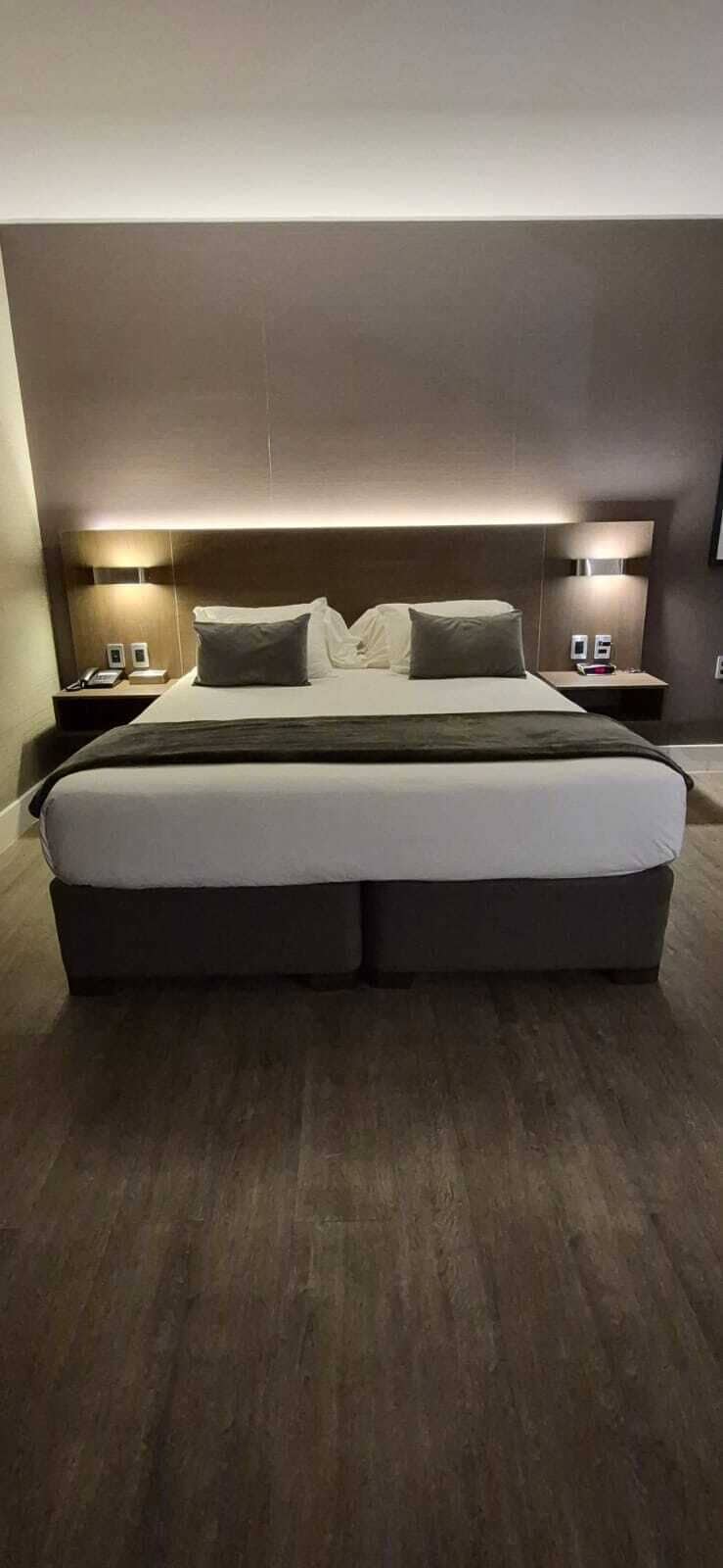 A modern hotel room with a large bed, two bedside tables, and wall-mounted lamps.