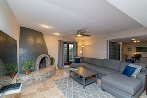 A living room with a stone fireplace, a gray sofa, a coffee table, and a ceiling fan. - Casa De Palms (Scottsdale)