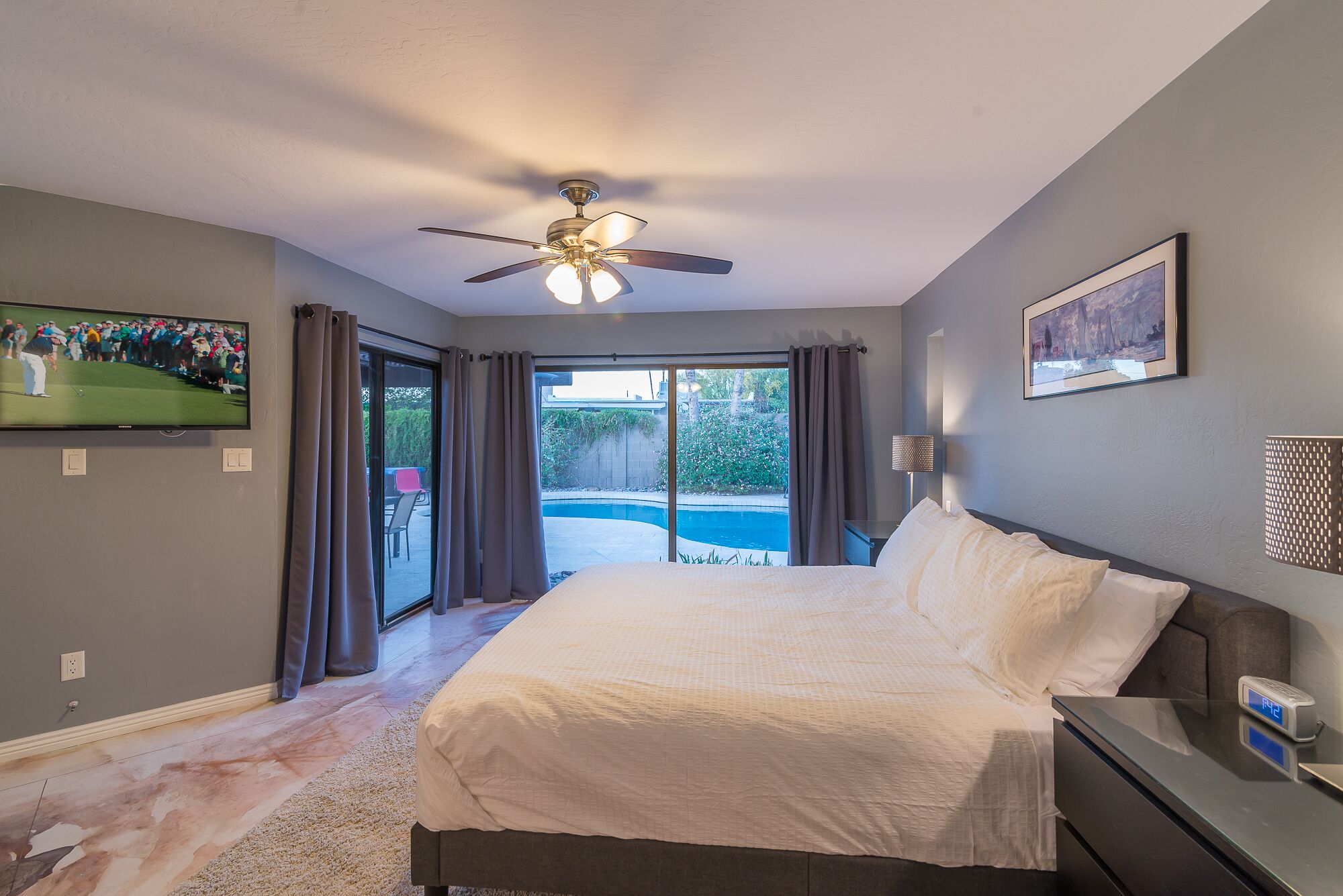 A bedroom with a bed, a ceiling fan, a TV, and a view of a swimming pool.