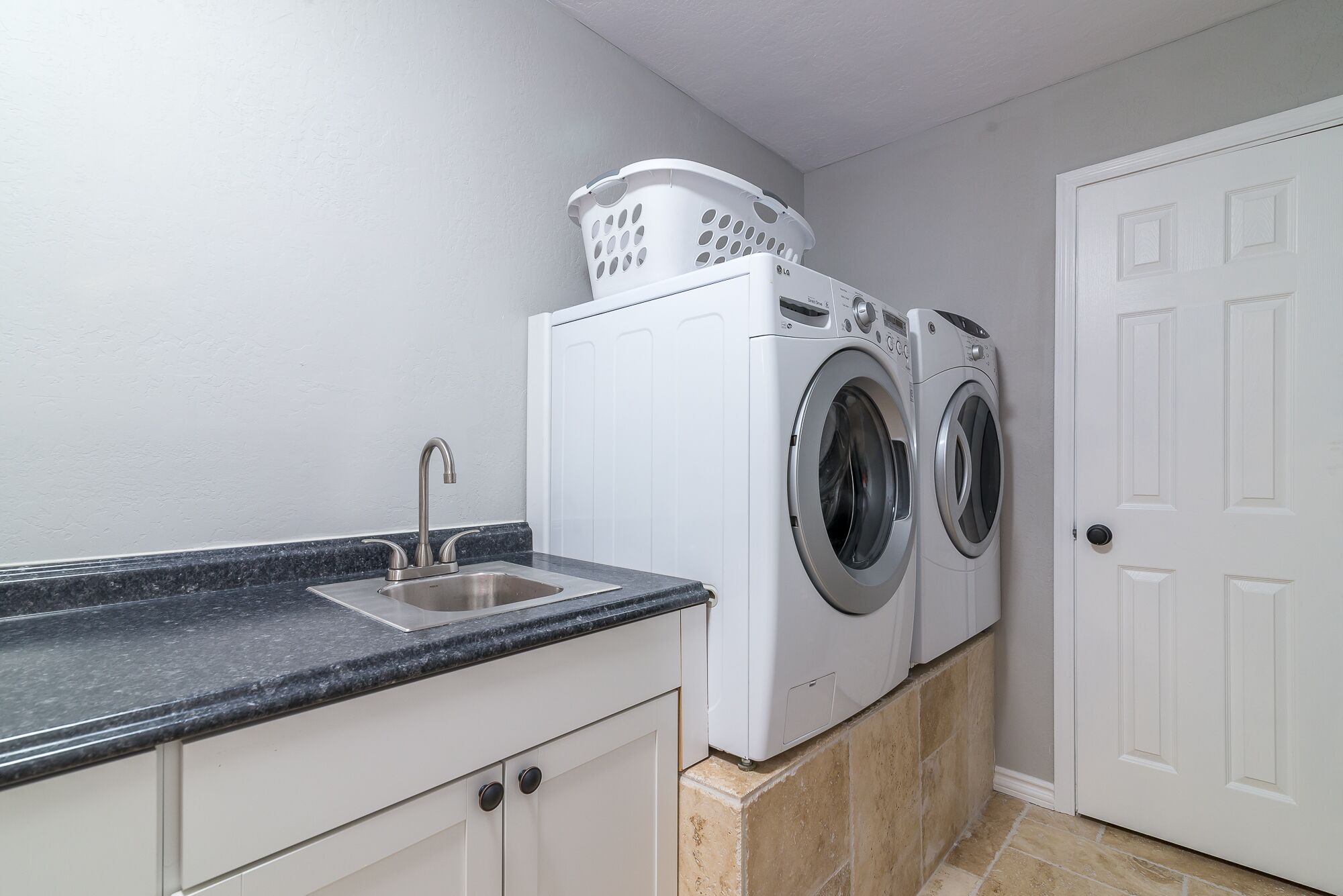 A laundry room with two front-loading washing machines, a sink, and a white door.