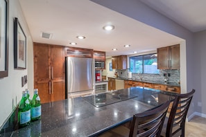 A modern kitchen with a central island, stainless steel appliances, wooden cabinets, and a large window providing natural light. - Casa De Palms (Scottsdale)