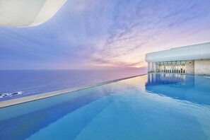Una piscina infinita moderna con una vista despejada del océano al atardecer.