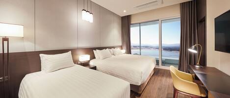 Quarto de hotel com duas camas, uma escrivaninha, uma cadeira e uma janela grande com vista para a cidade.