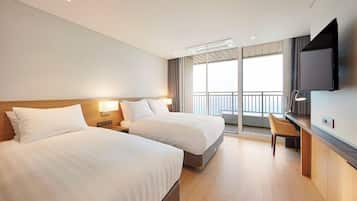 A hotel room with two beds, a desk, a chair, a TV, and a balcony with a railing.