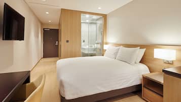A modern hotel room with a large bed, bedside table, a desk, and a TV mounted on the wall.