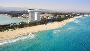 An aerial view of a coastal city with a prominent high-rise hotel, a sandy beach, and clear blue waters. - Skybay Hotel Gyeongpo (Gangneung)