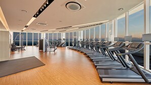 A modern gym with treadmills aligned along a wall with large windows offering a view of the sea. - Skybay Hotel Gyeongpo (Gangneung)
