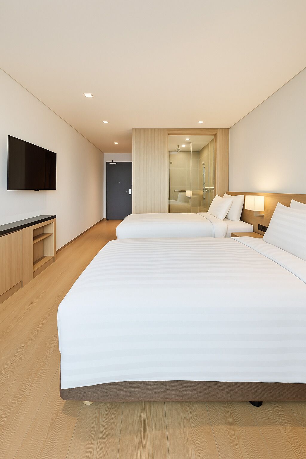 Ett modernt hotellrum med en stor säng, en TV, ett skrivbord och ett badrum som syns genom en glasdörr.
