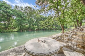 A stone bench by a river with a stone wall and trees in the background.