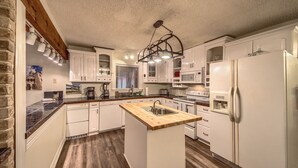 Una cocina con armarios blancos, una isla de madera con pileta, microondas integrado y refrigerador.