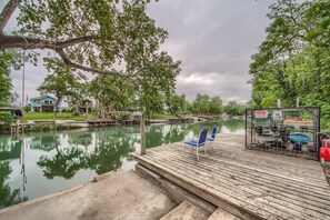A wooden dock with a blue chair, a calm river, and a house in the background.