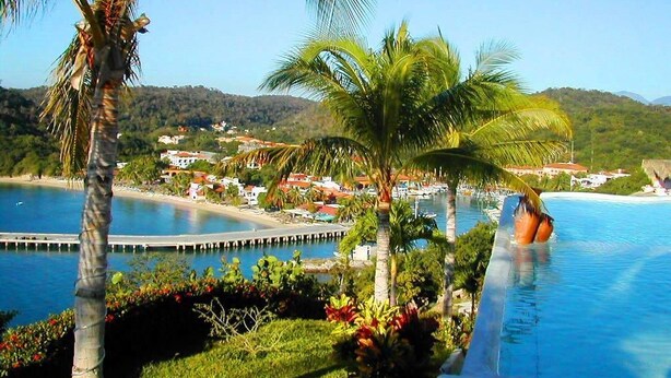 A resort with a swimming pool, palm trees, and a view of a coastal town. - Villa Punta Sta Cruz 3BR (Santa María Huatulco)