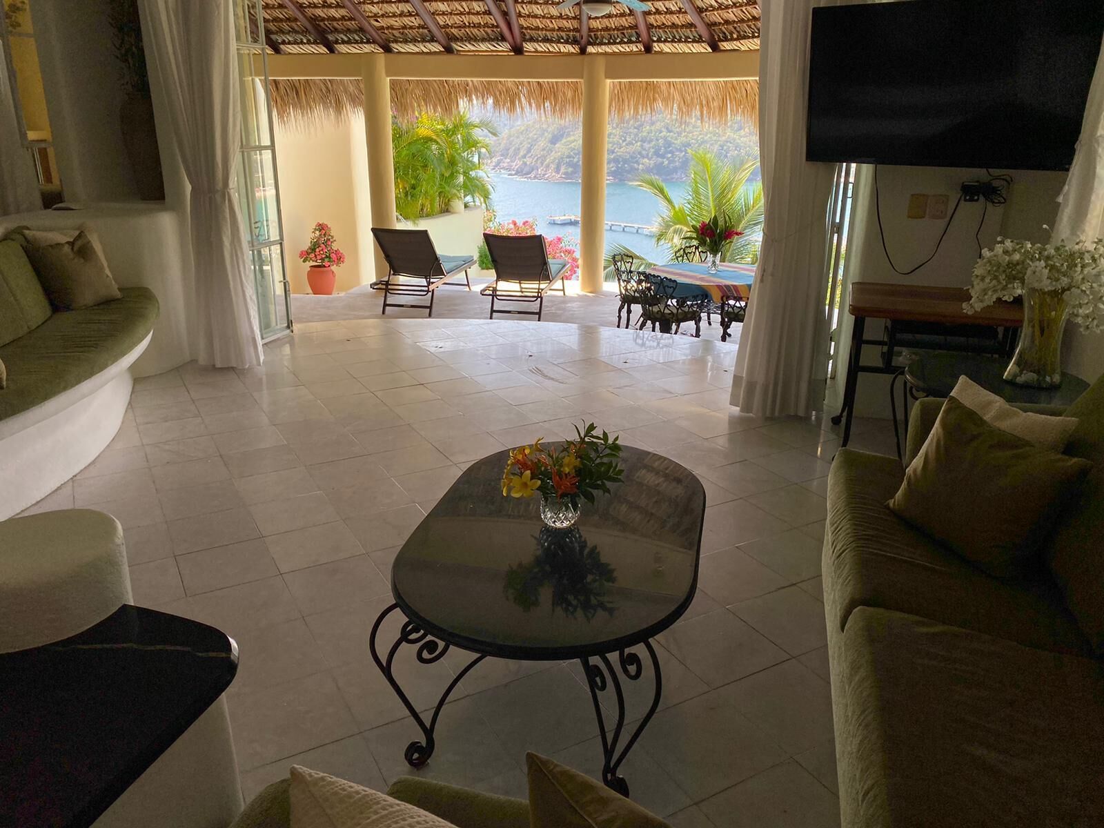 A spacious living area with a glass coffee table, comfortable seating, a TV, and a view of the sea.