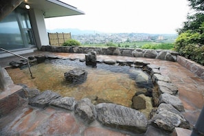 A hot spring area with a stone border and a view of a city in the background. - Breezbay Resort Yamaga (Yamaga)