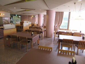 A restaurant with multiple tables and chairs, a large pillar, and a view of the outdoors through a window.