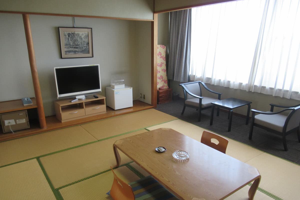 A traditional Japanese-style room with tatami flooring, a low table, and a television on a stand.
