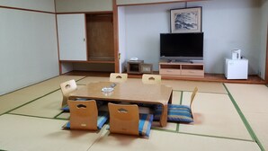 A traditional Japanese-style room with tatami flooring, a low wooden table with cushions, a television, and a small refrigerator.