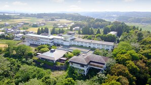 A large, modern building with multiple wings, surrounded by lush greenery and a rural landscape.