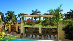A pool area with lounge chairs and a building with a thatched roof. - Condominio SDM Chahue 2BR (Santa María Huatulco)