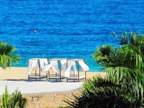 A beachside setting with a row of white-covered chairs and tables, palm trees, and a clear blue sea. - Condominio SDM Chahue 2BR (Santa María Huatulco)