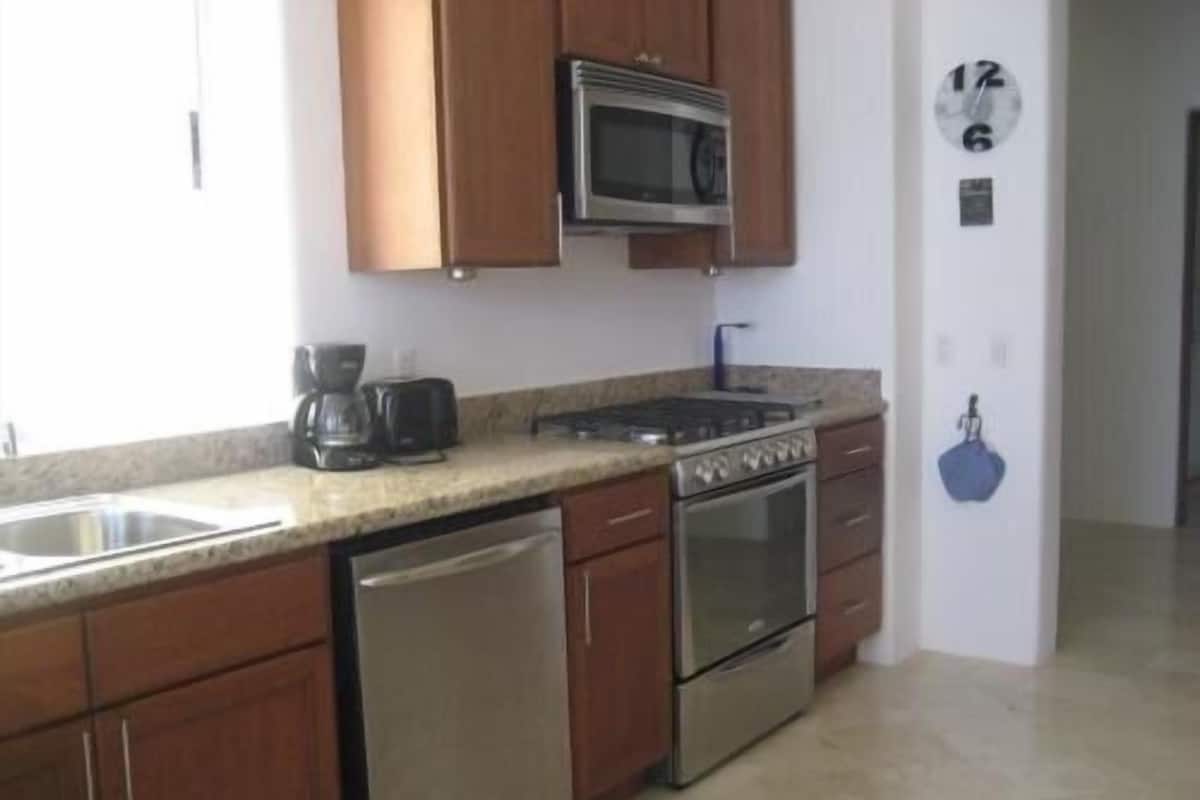 A kitchen with wooden cabinets, stainless steel appliances, a dishwasher, and a clock on the wall.