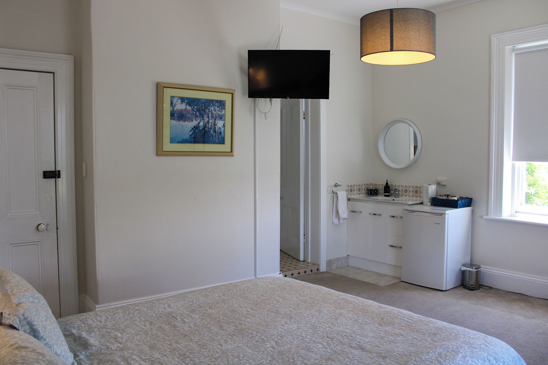 Un dormitorio con cama, televisor, baño con lavamanos y espejo, y una ventana.