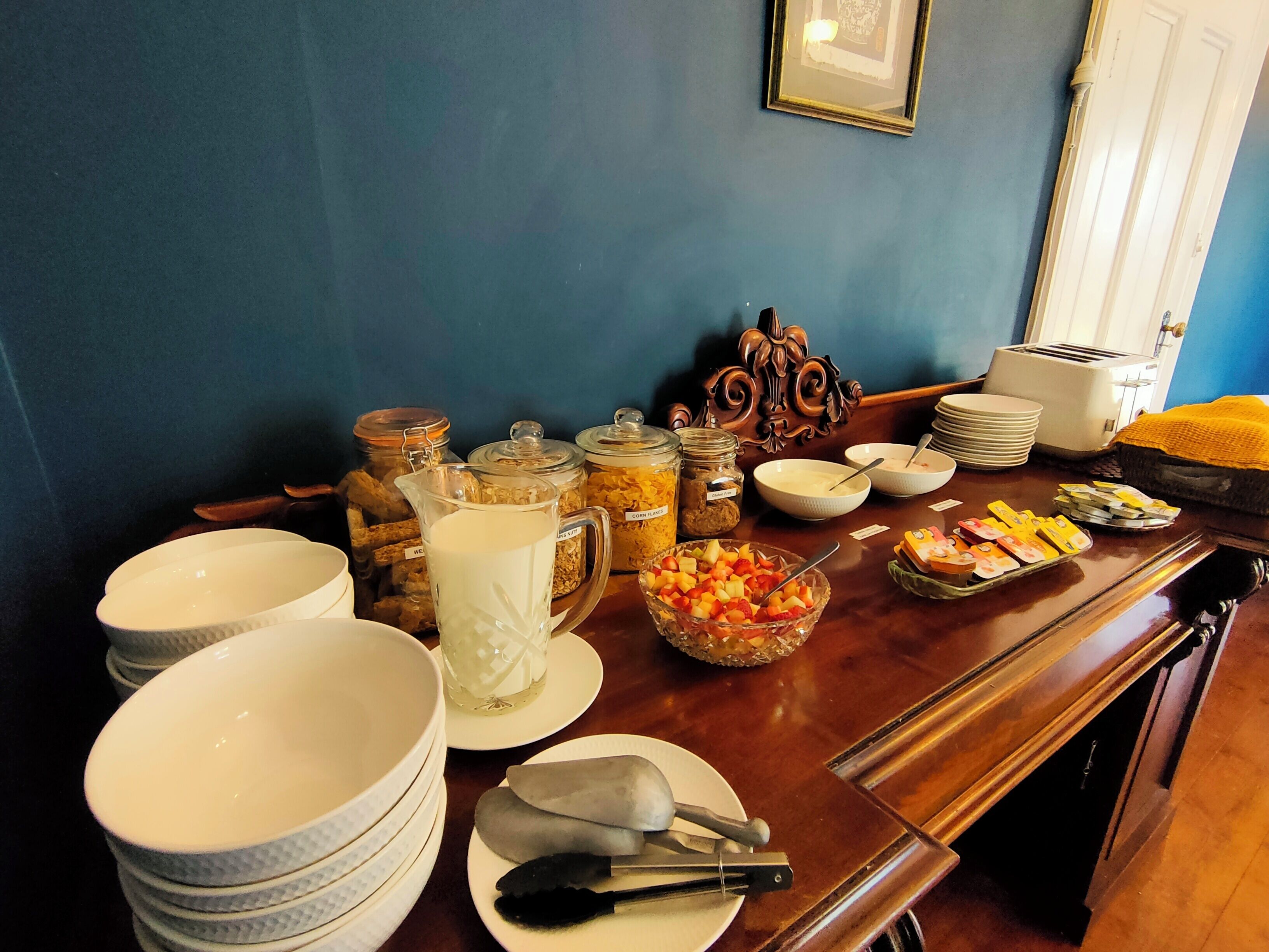 A breakfast buffet with various food items and utensils on a wooden table.
