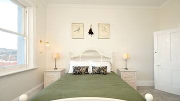 A bedroom with a bed, two bedside tables, a window, and two framed pictures on the wall.