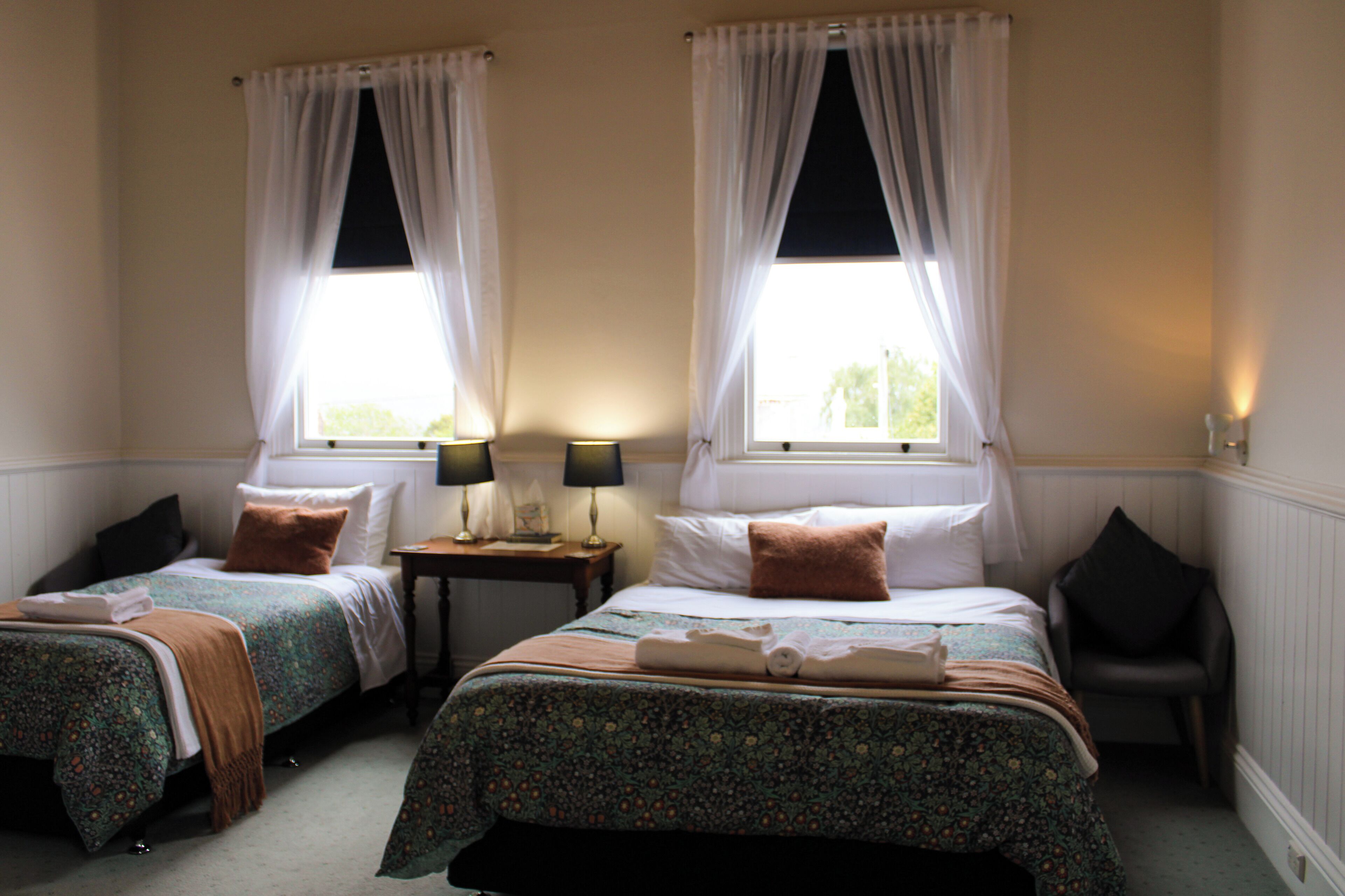 Une chambre double avec deux lits, chacun étant équipé d’un oreiller, d’une table de chevet, d’une lampe et d’une chaise.