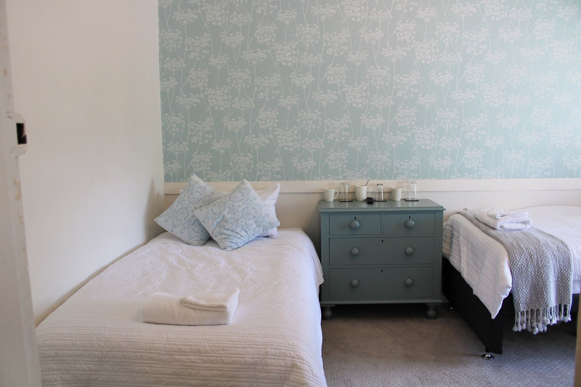 Un dormitorio con dos camas, un tocador y una pared con papel tapiz floral.