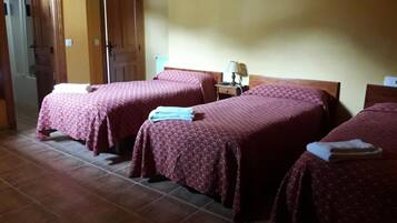 A hotel room with two beds, each with a red patterned bedspread and a folded towel on the side. There is a nightstand with a lamp between the beds.