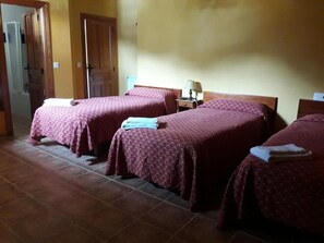 A hotel room with two beds, each with a red patterned bedspread and a folded towel on the side. There is a nightstand with a lamp between the beds. - Hotel Casa Vieja (Posada de Valdeon)