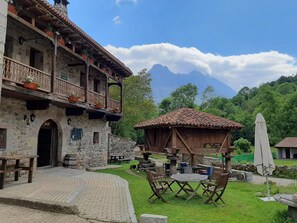 A rustic stone building with a bar, outdoor seating, and a view of mountains. - Hotel Casa Vieja (Posada de Valdeon)