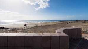 Una playa con una estructura de piedra curvada en primer plano, arena y cielo despejado.
